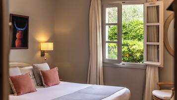 A bedroom with a bed, a nightstand, a lamp, a window with curtains, and a painting on the wall.