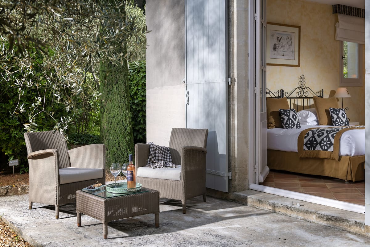 Une pièce comprenant un lit, deux chaises, une table avec un verre et une porte donnant sur un balcon.