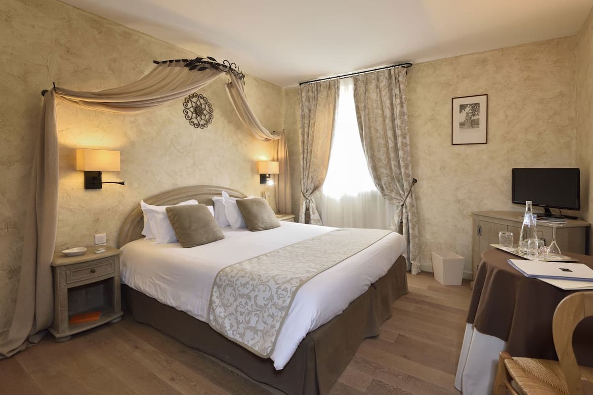 Une chambre d’hôtel avec un grand lit, deux tables de chevet, un bureau avec une chaise, une télévision et un tableau au mur.