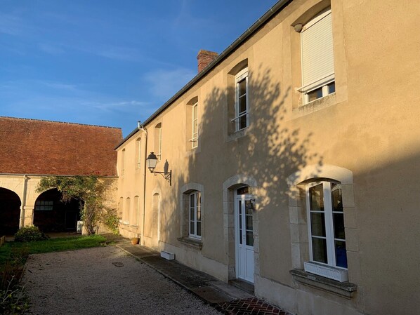 Un bâtiment avec une allée gravillonnée, un arc en briques et une façade traditionnelle dotée de nombreuses fenêtres et d’une porte.