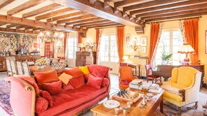 A spacious living room with a red sofa, yellow armchair, and a wooden coffee table. There is a piano and a bookshelf in the background. - Le Petit Manoir Des Bruyeres (Villefargeau)
