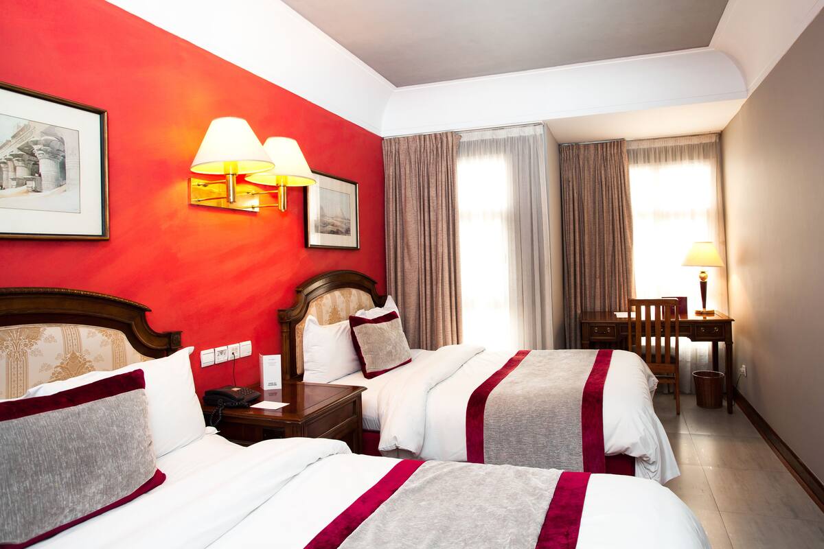 Habitació d'hotel amb dos llits, un escriptori, una cadira i una làmpada.