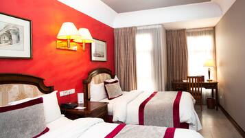 A hotel room with two beds, a desk, a chair, and a lamp.