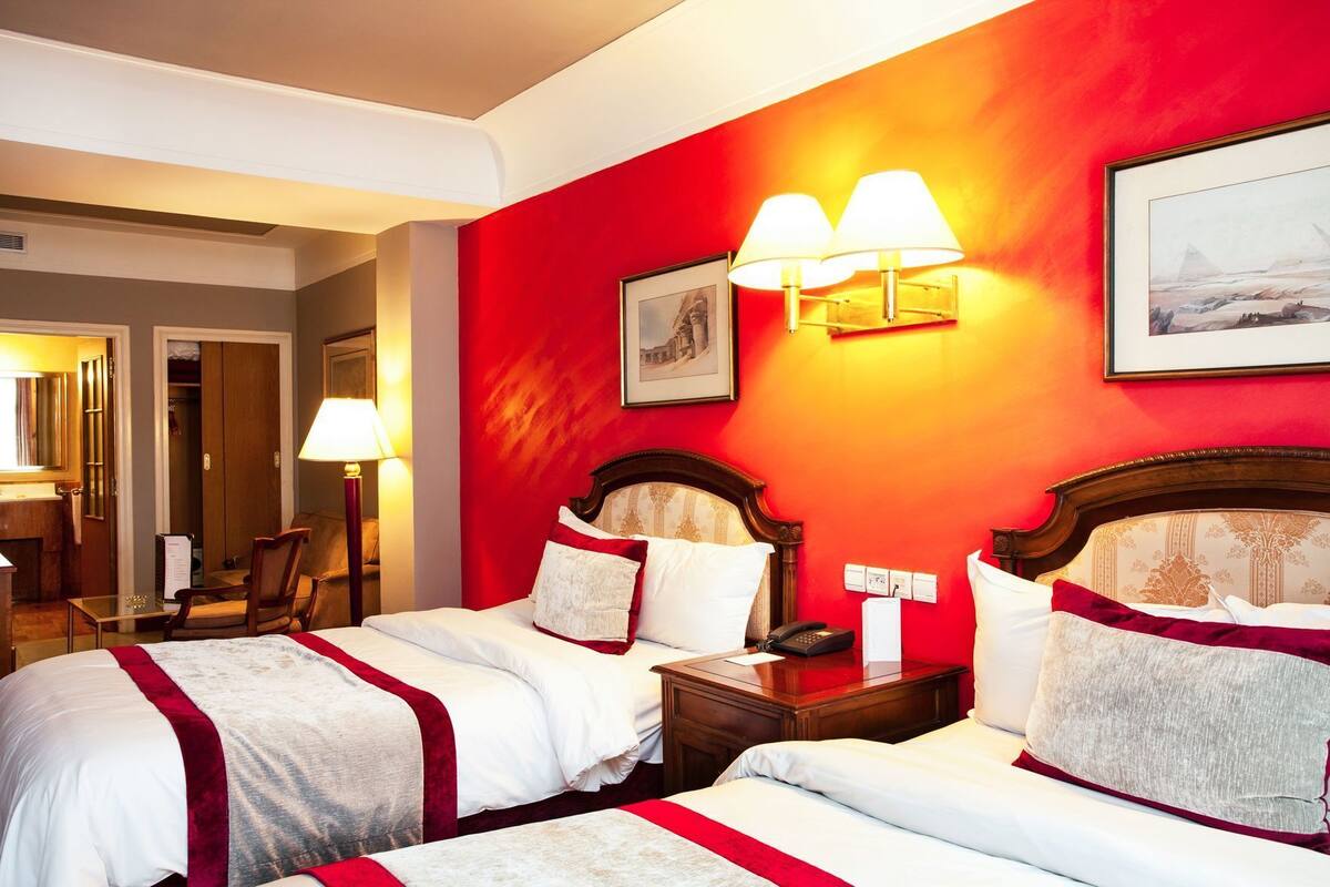 Habitació d'hotel amb dos llits, una paret vermella decorativa i un quadre encimbellat sobre els llits.