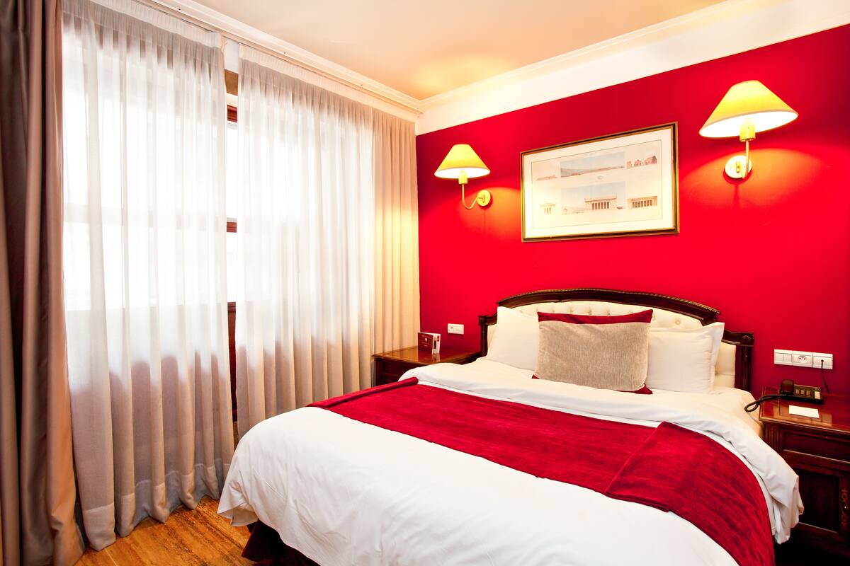 Habitació d'hotel amb un llit gran, parets vermelles i dues làmpades al costat del llit.