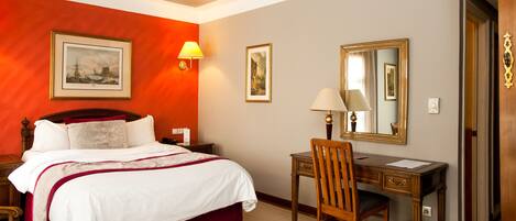 A hotel room with a bed, desk, chair, and a mirror.