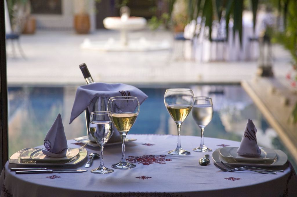 Mesa de comedor con cuatro copas de vino, una botella y un cono de servilletas, frente a una vista de la piscina.