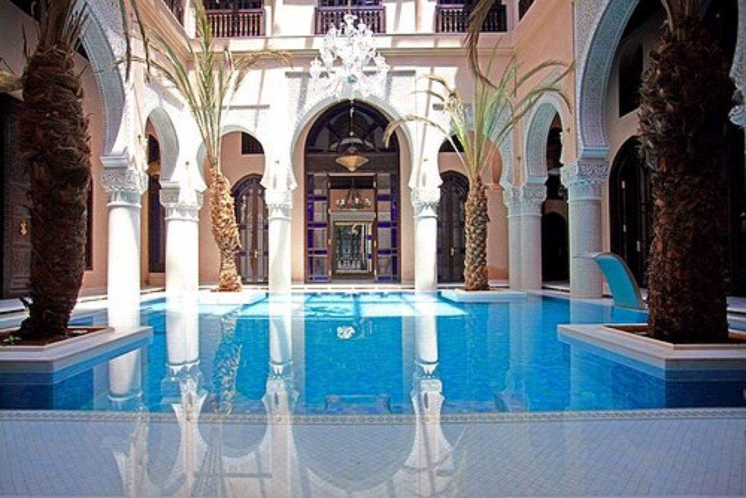 A pool area with a central water feature, surrounded by arches and palm trees.