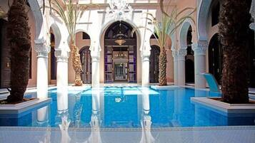 A pool area with a central water feature, surrounded by arches and palm trees.