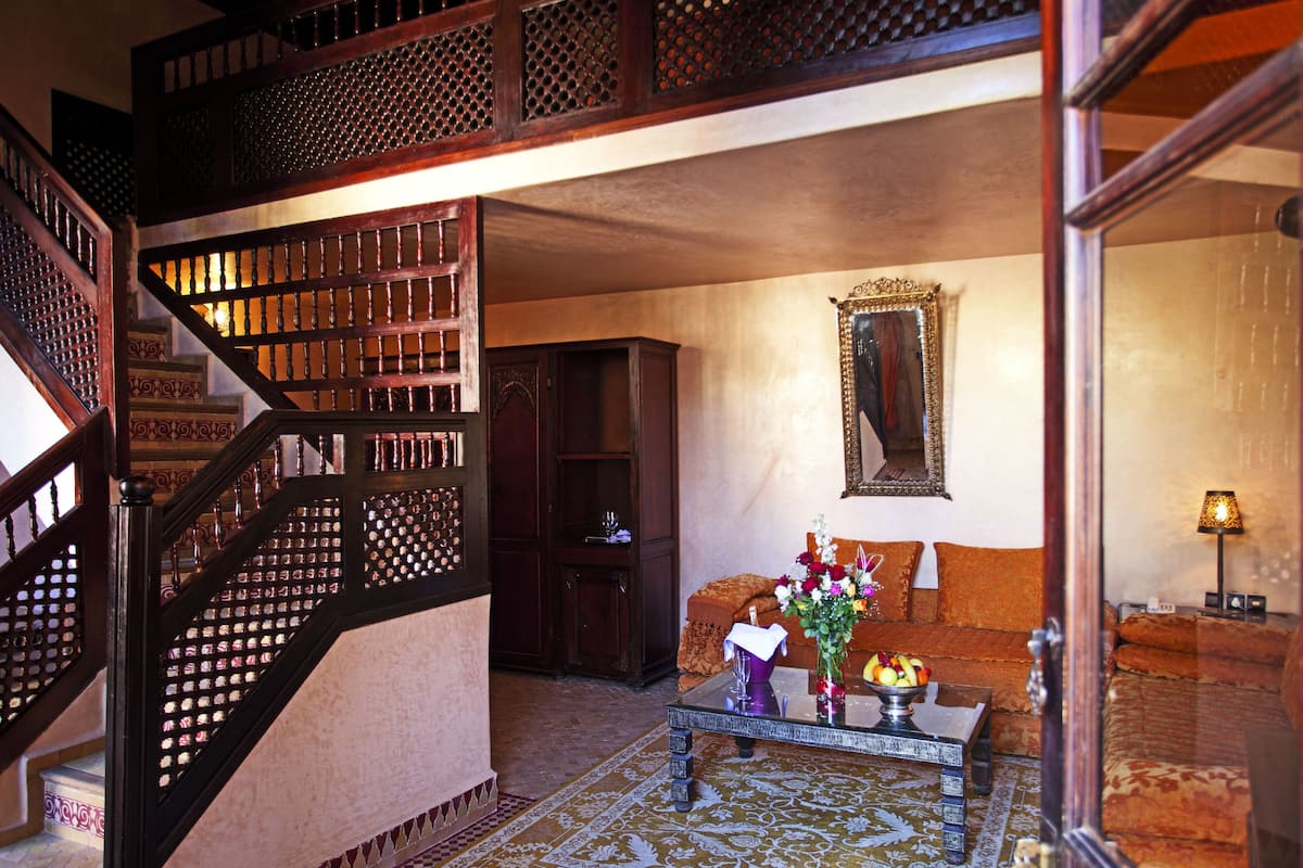 Un interior tradicional con una escalera de madera, un conjunto de sofás, una mesa de centro con un jarrón y un espejo en la pared.