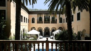 Un patio con piscina, palmeras y un edificio con arcos y columnas.