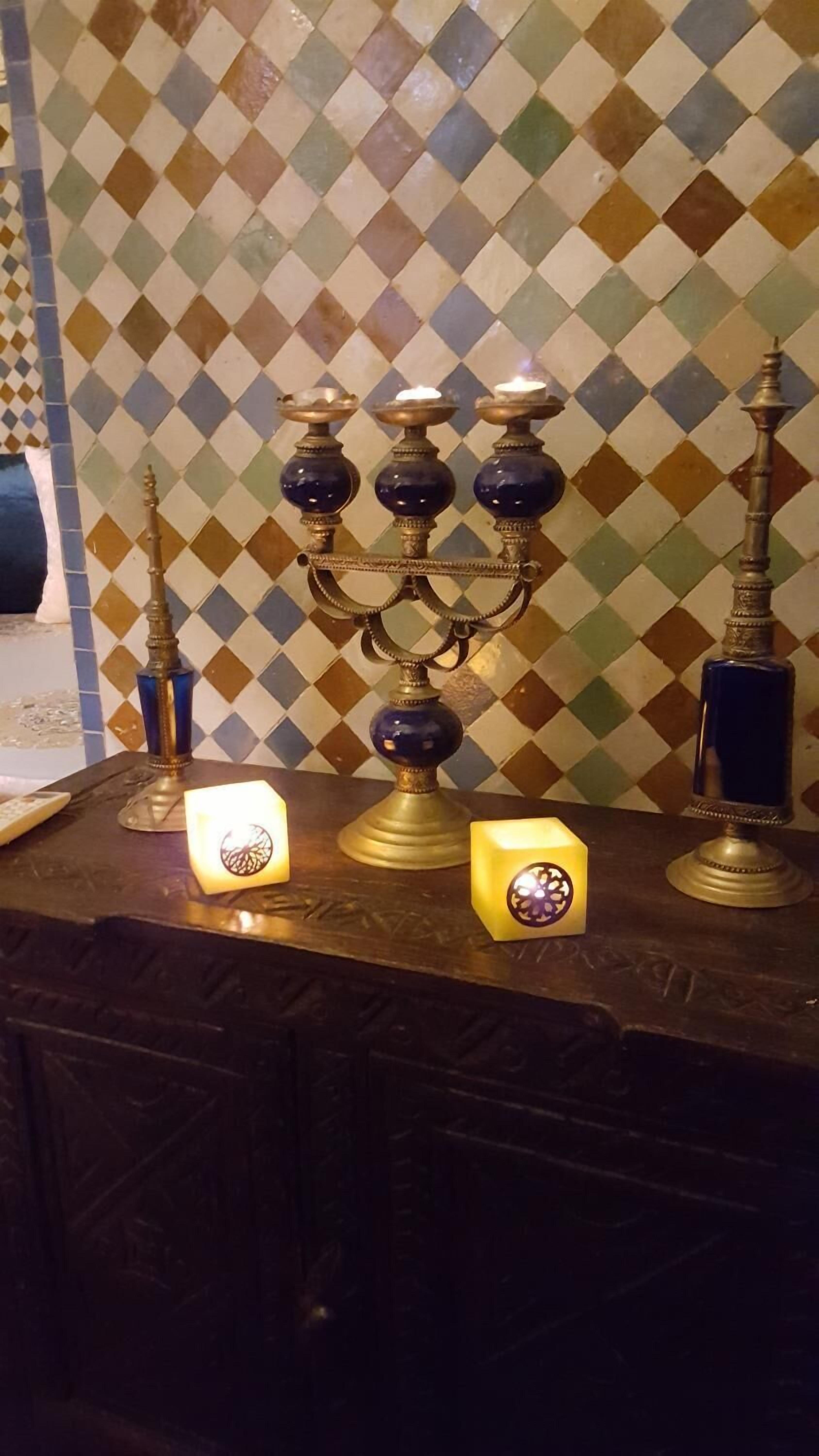 Un chandelier traditionnel en laiton, orné de plusieurs bougies, une bouteille bleue et deux bougies allumées, le tout posé sur une surface en bois.