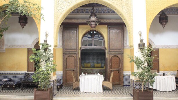 An ornate entrance with a tiled floor, a wooden door, and a bench outside. - Palais Didi (Meknes)