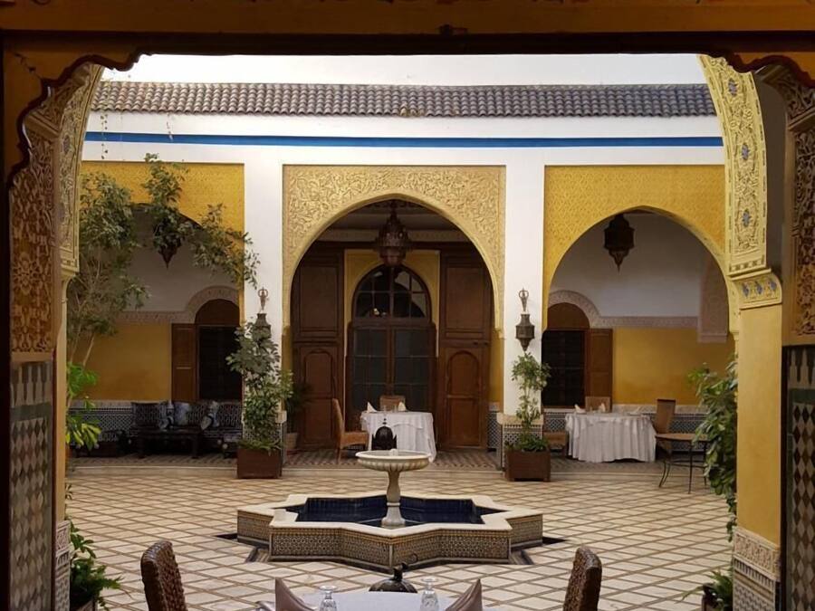 An indoor courtyard with a round table and chairs, surrounded by arches and potted plants.