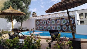 A pool area with lounge chairs and umbrellas, surrounded by a decorative tiled wall. - Palais Didi (Meknes)