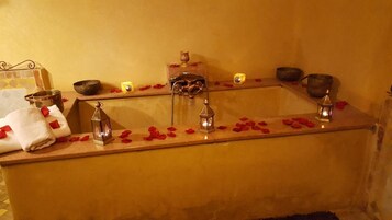 Una bañera con pétalos de rosa, una lámpara pequeña y un adorno en el borde.