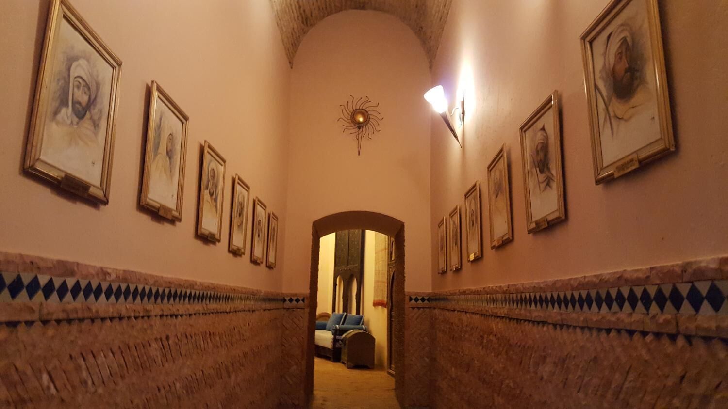 Un pasillo con retratos enmarcados en las paredes, una alfombra estampada y un acceso a una habitación.