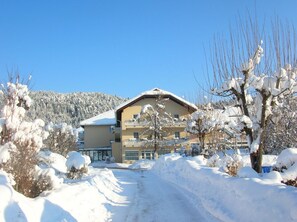 Een met sneeuw bedekt gebouw met een balkon, omgeven door bomen en een heldere lucht.