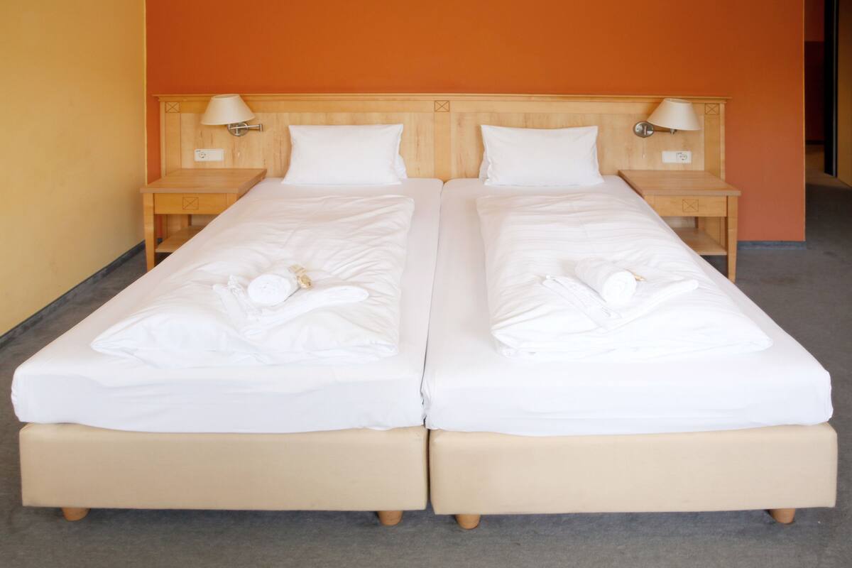 Un lit double avec deux tables de chevet, chacune équipée d’une lampe, dans une chambre aux murs orange.