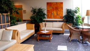 A lobby with wicker furniture, a coffee table, and large potted plants.