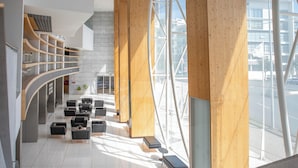 A modern lobby with a curved staircase, wooden columns, and a seating area with black chairs and tables.