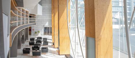 A modern lobby with a curved staircase, wooden columns, and a seating area with black chairs and tables.