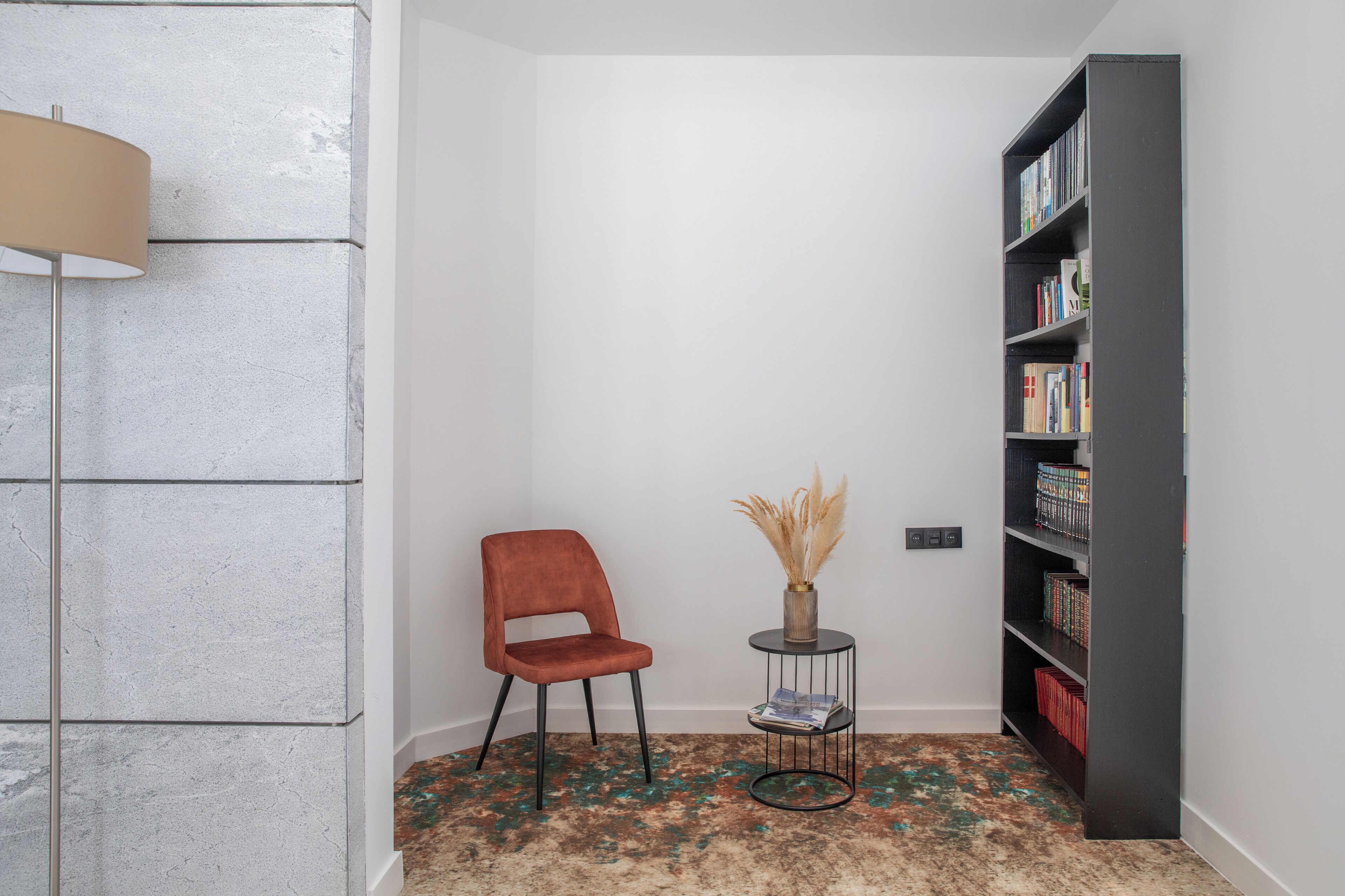 A room with a red chair, a small round table with a vase, and a bookshelf.