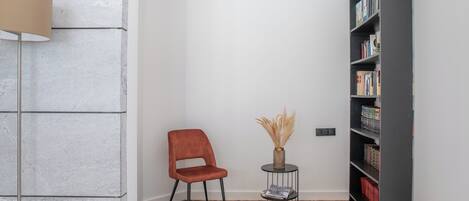 A room with a red chair, a small round table with a vase, and a bookshelf.