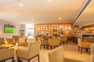 Un vestíbulo de hotel con zonas de estar, un bar y un televisor que muestra un evento deportivo.