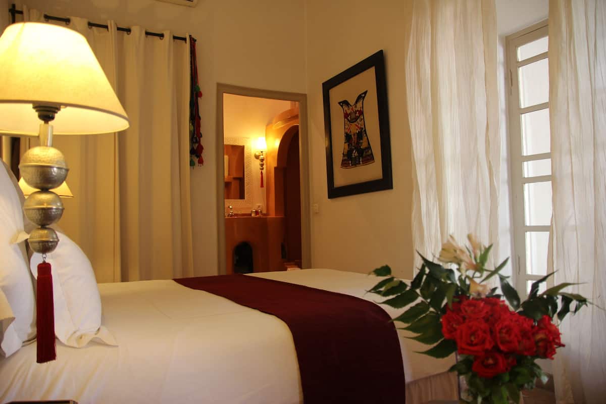 A hotel room with a bed, a lamp, a framed picture on the wall, and a window with curtains.