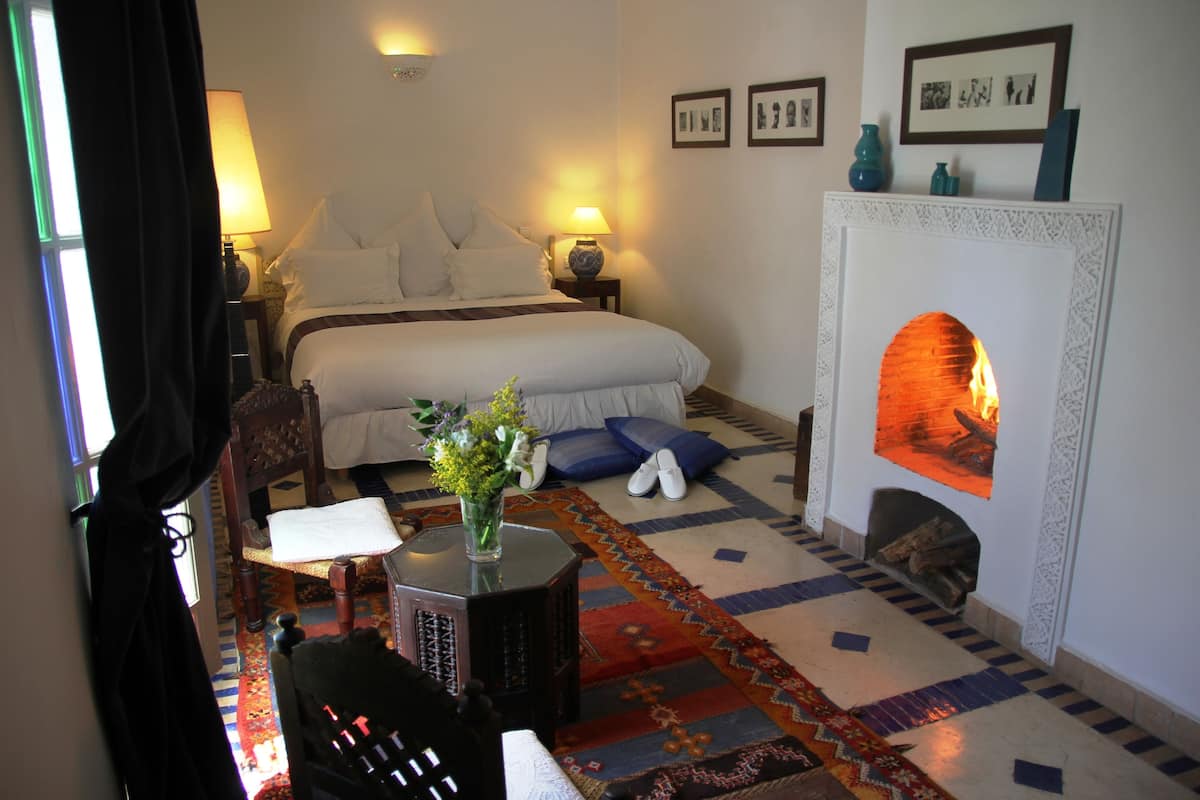 A hotel room with a large bed, a fireplace, a carpeted floor, and a nightstand with a lamp.
