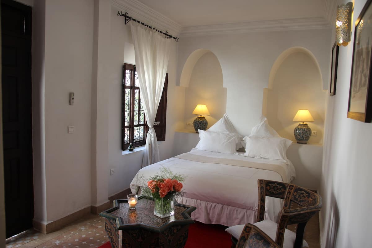 A hotel room with a bed, two bedside lamps, a table with a candle, and a vase of flowers.