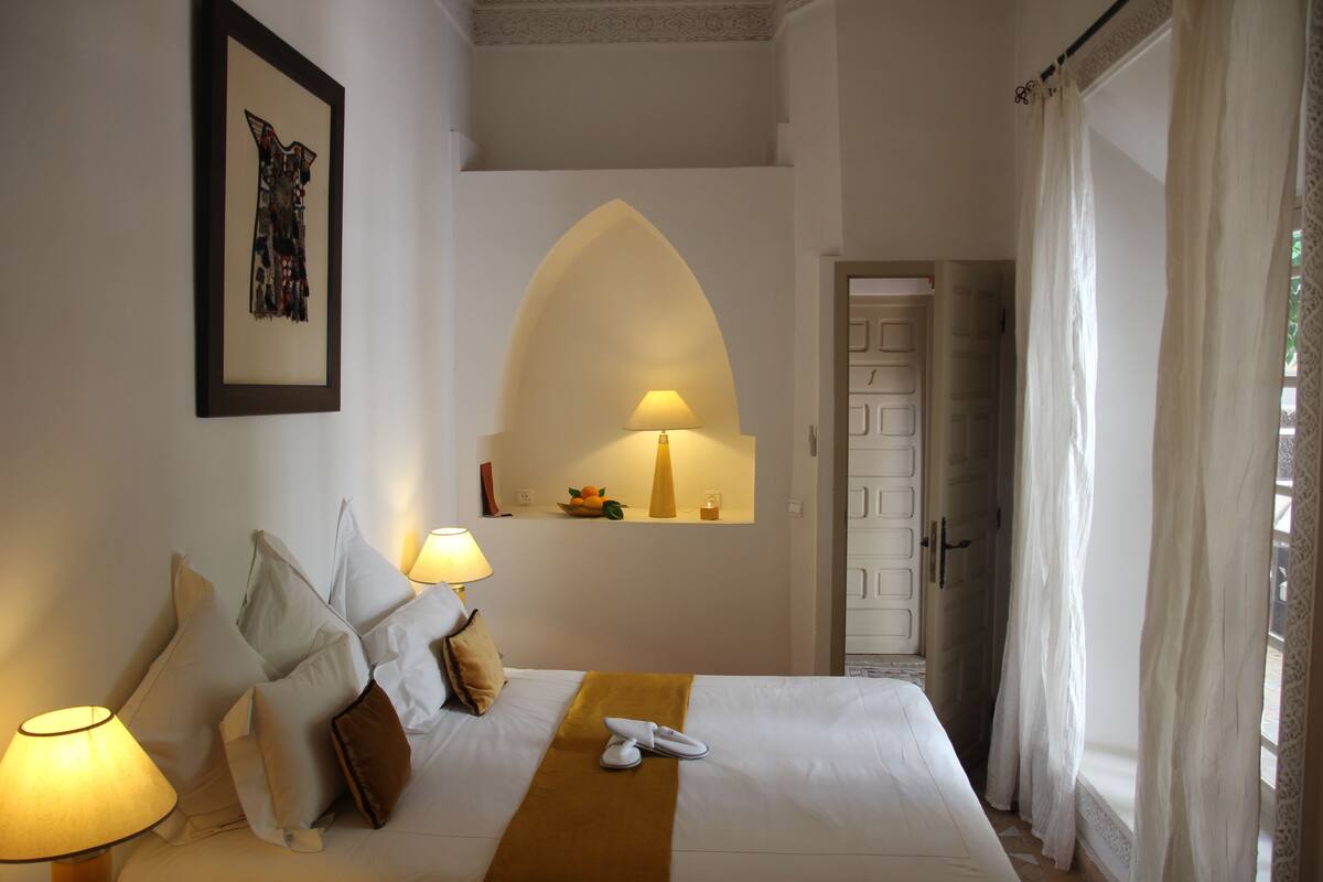A hotel room with a bed, pillows, a lamp, a framed picture, and a door.