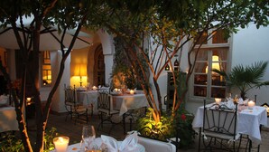An outdoor dining area with tables set for a meal, surrounded by greenery and candlelight. - Riad Clémentine (Marrakech)