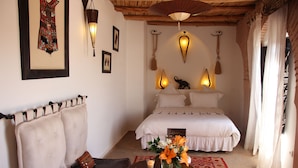 A bedroom with a bed, a nightstand, a chair, a table with a vase of flowers, and wall-mounted lights. - Riad Clémentine (Marrakech)