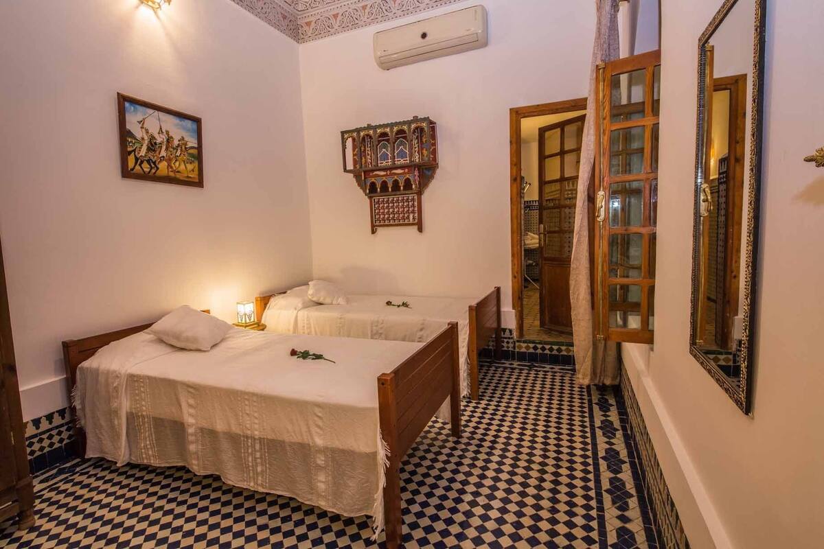 Una habitación con dos camas de madera, un espejo grande y un suelo a cuadros.