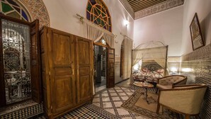 A traditional Moroccan interior with wooden doors, a checkered floor, a patterned rug, and a cushioned chair. - Riad Sara (Fes)