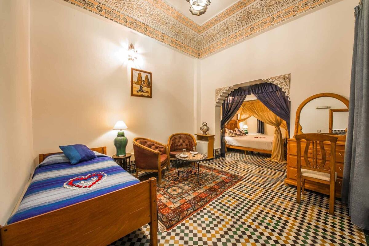 Una habitación con una cama, una silla, una mesita con una lámpara y una alfombra decorativa.