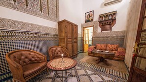 A traditional Moroccan interior with a patterned tile floor, a leather armchair, a wooden cabinet, and a sofa with cushions. - Riad Sara (Fes)