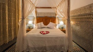 A bed with a canopy, a heart-shaped decoration on the bed, and patterned walls. - Riad Sara (Fes)