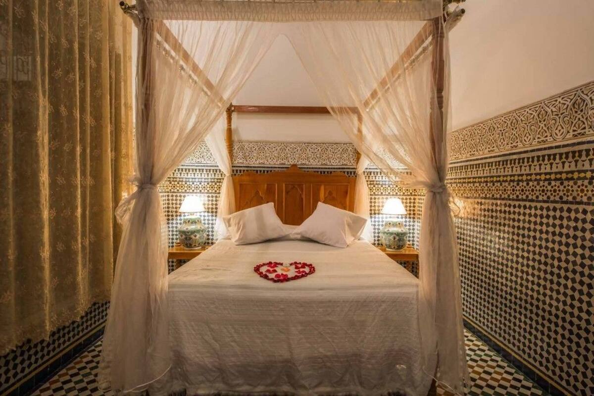 Una cama con dosel, una decoración con forma de corazón en la cama y paredes con estampado.