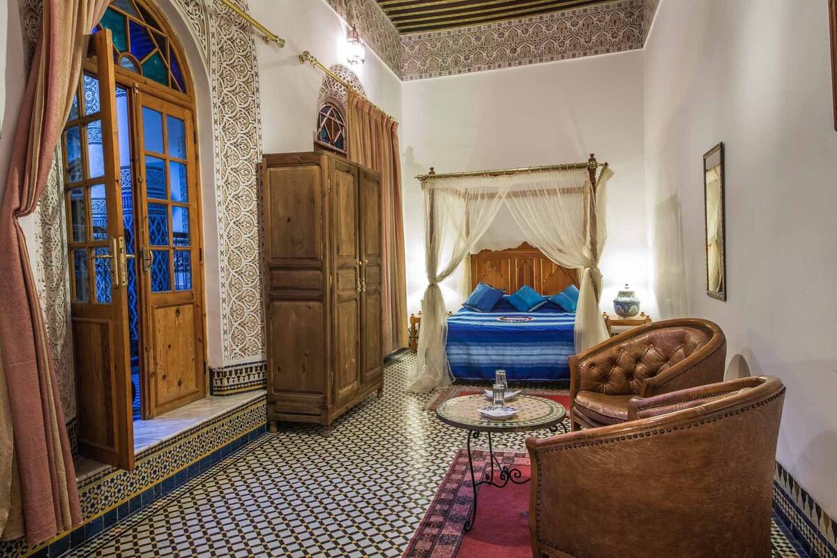 Una habitación tradicional marroquí con una cama, un armario de madera, una silla y una mesita.