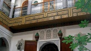 A traditional interior with ornate arches, wooden doors, and a balcony with decorative railings. - Riad Sara (Fes)