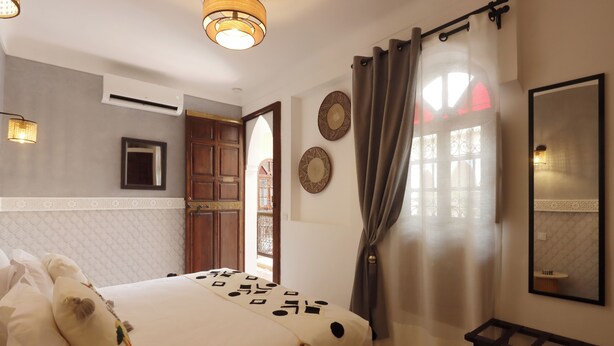 Una habitación de hotel con cama, espejo, armario y ventana con cortinas.