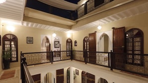 Un interior de varios niveles con arcos, un balcón con barandilla de hierro forjado y un candelabro.