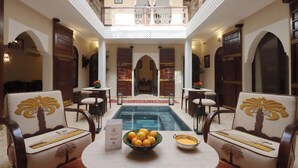 Zona de piscina con dos sillas, una mesa con un frutero y un cartel de menú.