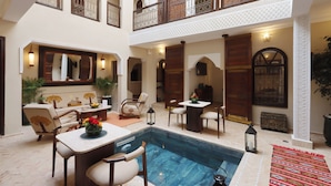 Amplio espacio interior con piscina, varios conjuntos de asientos y un balcón con barandilla ornamental.