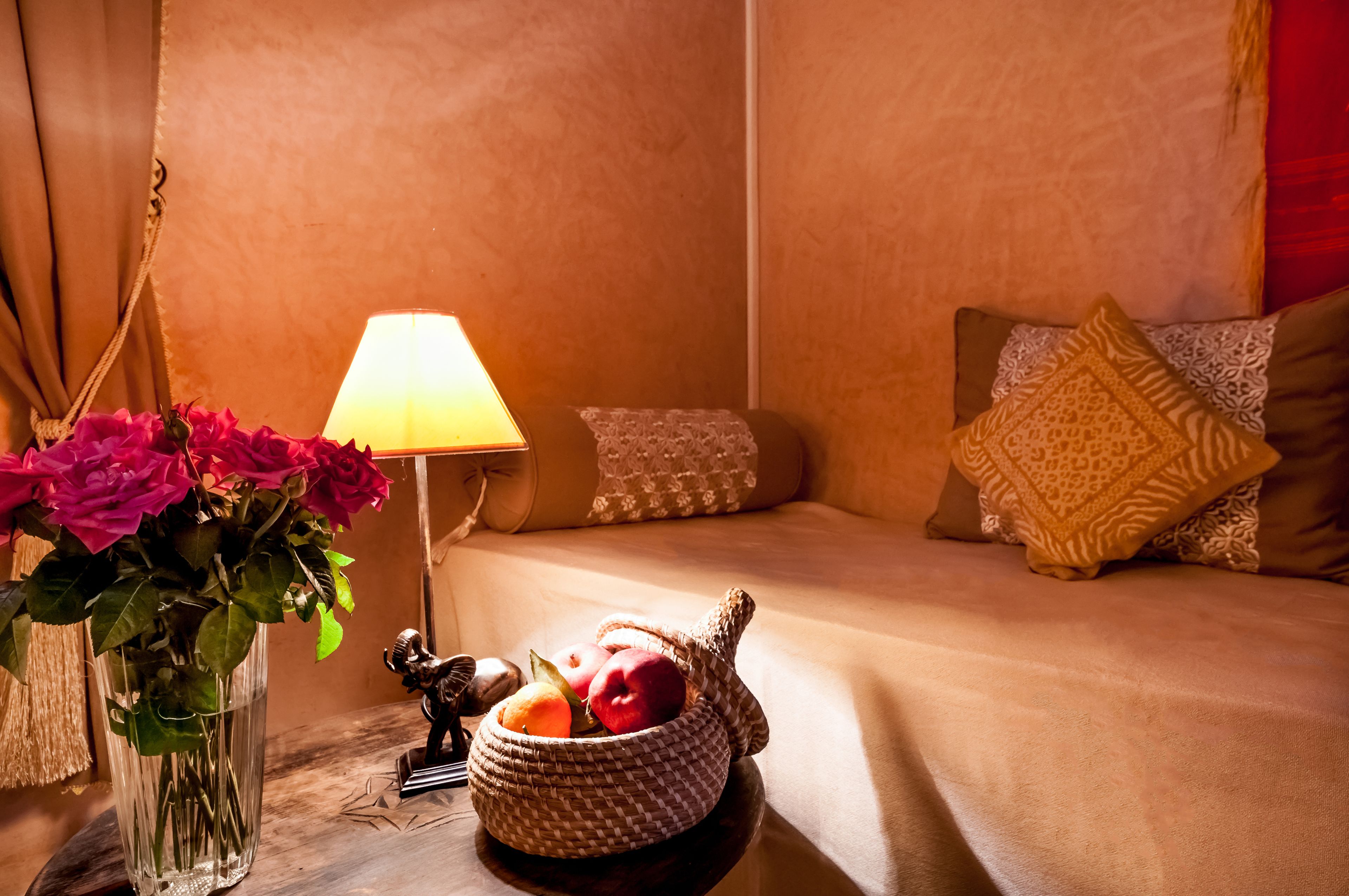 A cozy room with a bed, a lamp, a vase with flowers, and a basket of fruit.