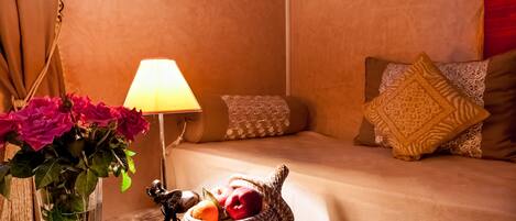 A cozy room with a bed, a lamp, a vase with flowers, and a basket of fruit.