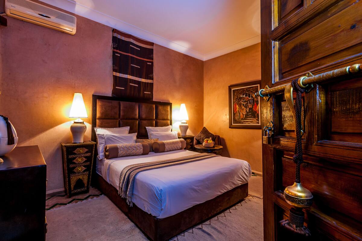 Habitación de hotel con una cama grande, dos mesitas de noche con lámparas, un armario de madera y un aire acondicionado instalado en la pared.